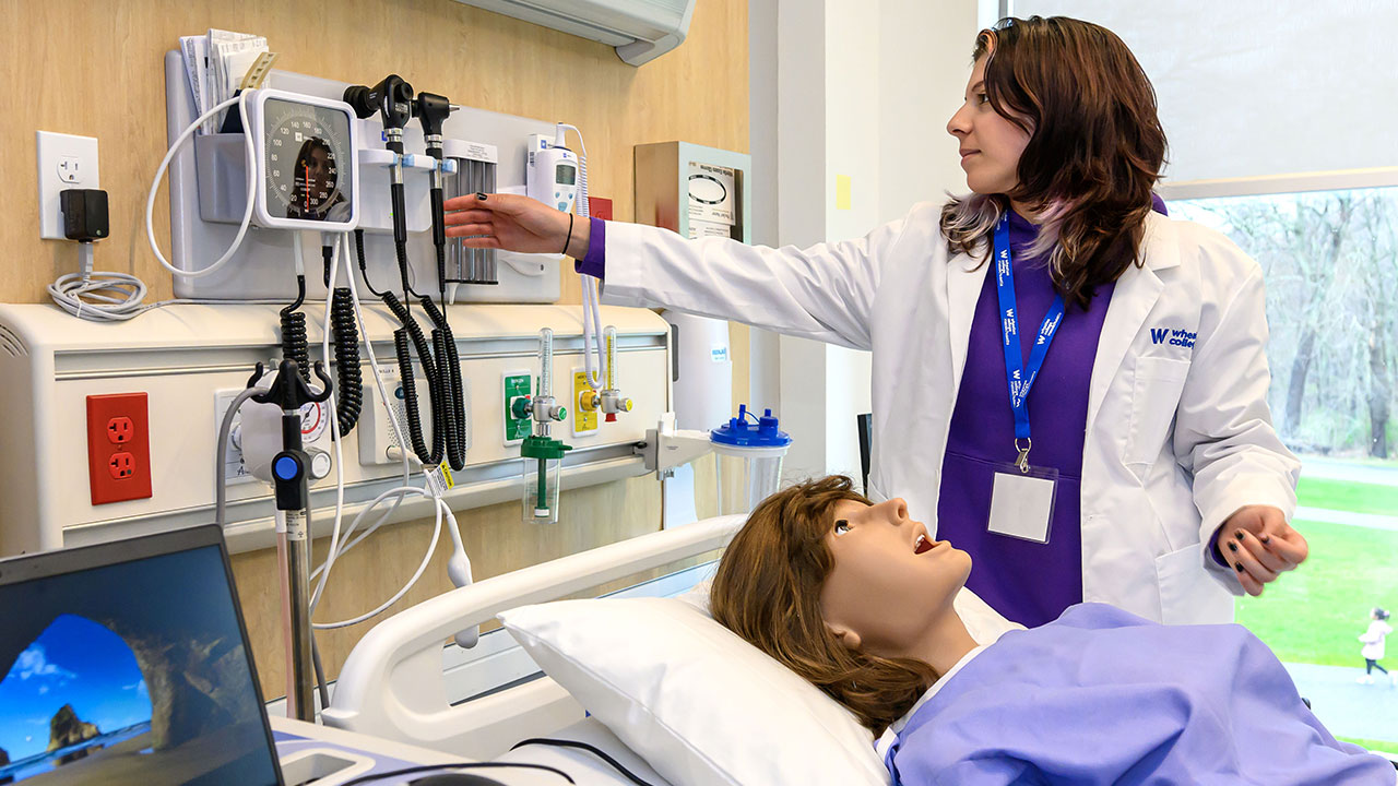 Nursing student in Wheaton's nursing labs working with a pretend patient.
